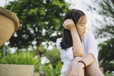 Bir parkta oturan üzgün Genç Asyalı kadın.