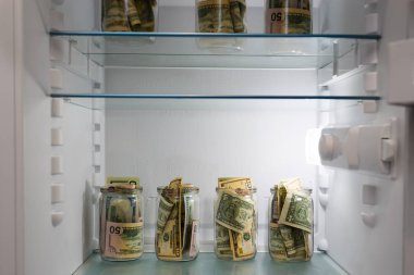 Dollars in a glass jar in the refrigerator. Saving money. Concept photo. clipart