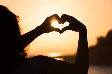 Günbatımı gökyüzü arka plan üzerinde parmak kalbinde