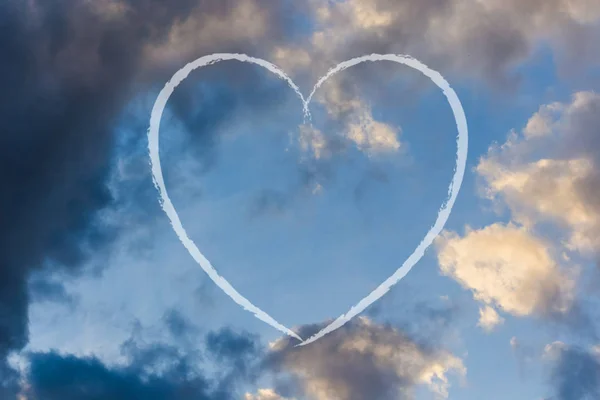 The trace of the plane in the form of heart against the sky with clouds