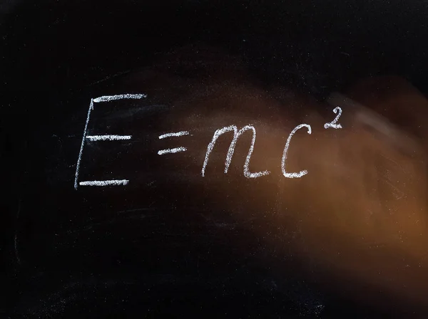 Einstein\'s theory formula written in chalk on a chalkboard with a velocity-blurred hand