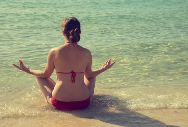 Lotus bulunduğu sahilde oturan ve bir mayo yoga yaparken kız