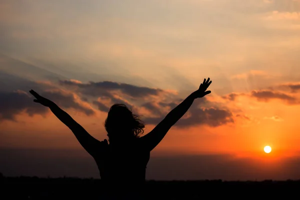 Silhouette of a girl at sunset with hands raised happily