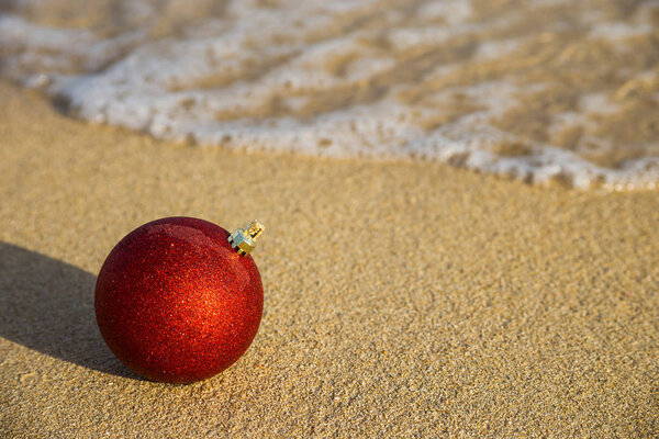 Red Christmas ball on the sand of the sea