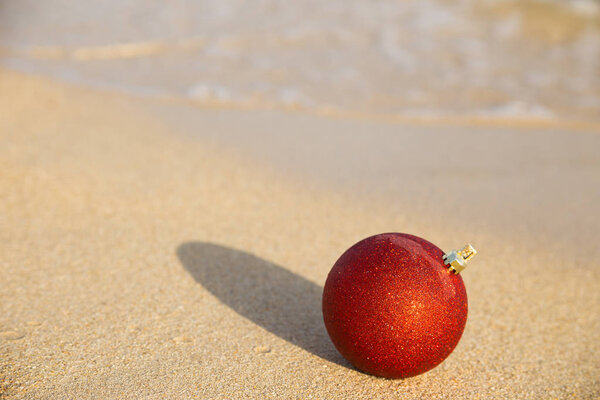 Red Christmas ball on the sand of the sea