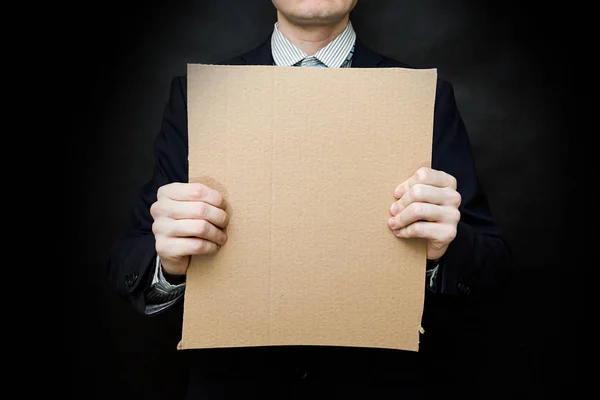 A man in a suit and tie with an empty cardboard on a dark background for the copy space for the inscription