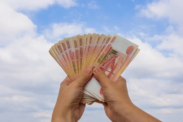 Egy csomag pénz a kézben szemben az eget felhők — Stock Fotó