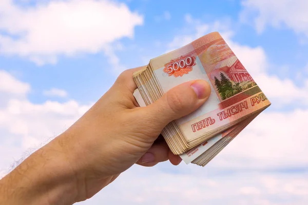 Un paquete de dinero en la mano contra el cielo con nubes — Foto de Stock