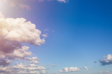 mavi gökyüzünde bulutlar, karşısında güneş tarafından aydınlatılan kabarık bulutlar