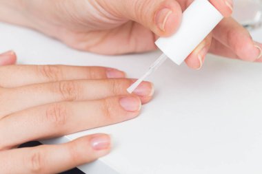 Beyaz bir arka plan üzerinde tırnaklar üzerinde net vernik koyarak