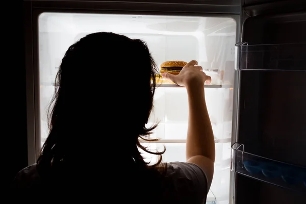 The girl reaches for harmful food in the fridge