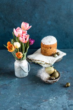 Paskalya kompozisyonu. Mavi dokulu taş arka plan üzerinde bir vintage kova lale bir buket, Paskalya yumurtası, Paskalya kek ve söğüt boyalı. Yakın çekim.