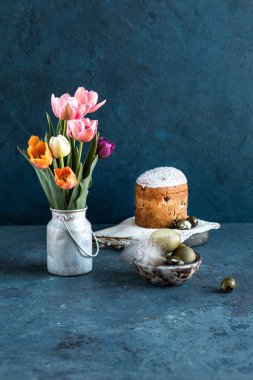 Paskalya kompozisyonu. Mavi dokulu taş arka plan üzerinde bir vintage kova lale bir buket, Paskalya yumurtası, Paskalya kek ve söğüt boyalı. Yakın çekim.