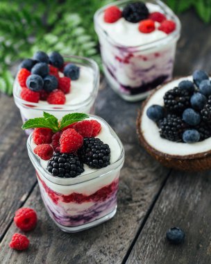 Ahududu, yaban mersini, koyu ahşap rustik arka plan üzerinde böğürtlen ile 3 bardak yoğurt. 