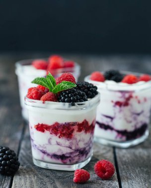 Ahududu, yaban mersini, koyu ahşap rustik arka plan üzerinde böğürtlen ile 3 bardak yoğurt. 