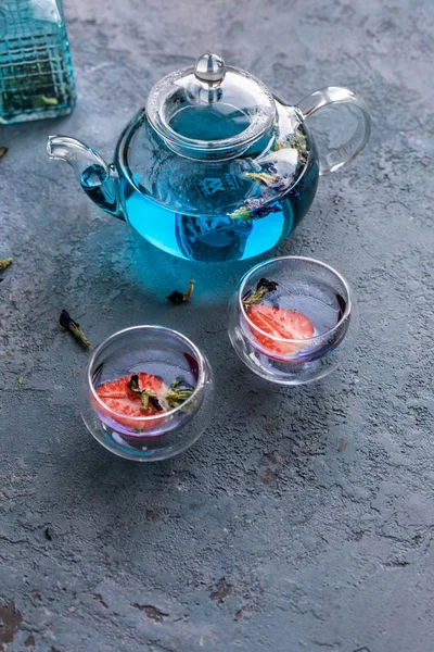 Mavi asya çayı 2 fincan ile çaydanlık. Çay fincanlarında strowberries. Kahverengi dokular taş arka plan.  