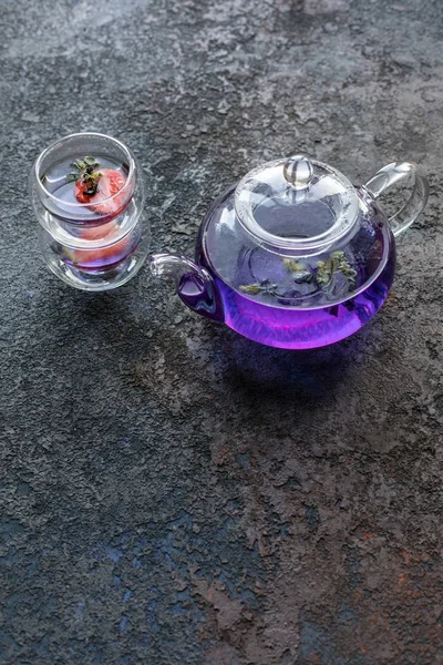 Asya menekşe çayı 2 fincan ile çaydanlık. Çay fincanlarında strowberries. Kahverengi dokular taş arka plan.  