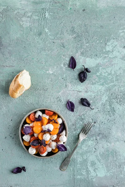 Fesleğenli yeşil mozzarella salatası, domates kiraz, limonlu bir bardak su. gri beton dokusal arka plan. Üstte görüntü.