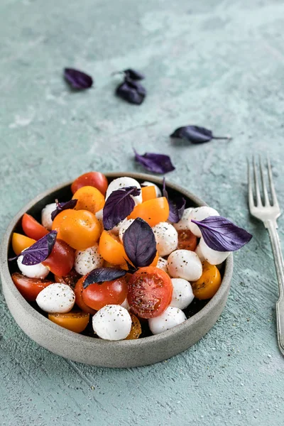 Fesleğenli yeşil mozzarella salatası, domates kiraz, limonlu bir bardak su. gri beton dokusal arka plan. Üstte görüntü.