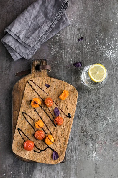Domates kiraz, fesleğen, gri taş arka plan üzerinde balsamik ile pide ekmek. Bir bardak limonlu suyla. Üstte görüntü.