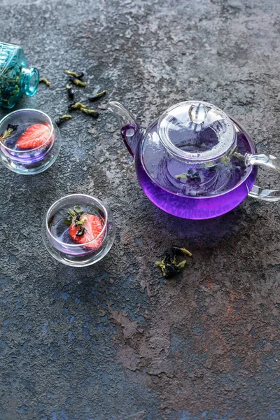 Menekşe asya çayı 2 fincan ile çaydanlık. Çay fincanlarında strowberries. Dokulu taş kahverengi arka plan.