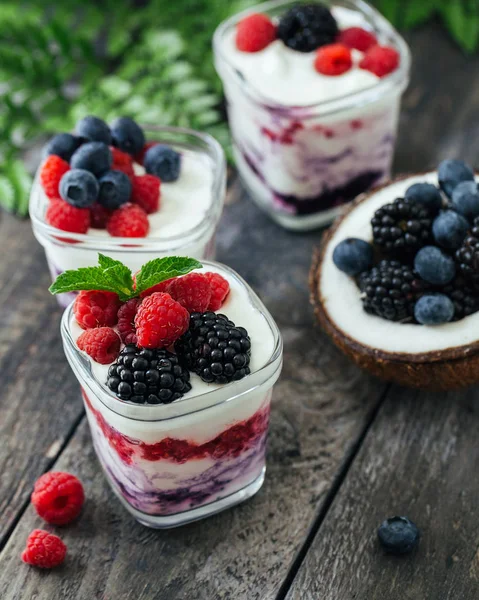 3 cups yogurt with raspberries, blueberries, blackberries on a dark wooden rustic background.