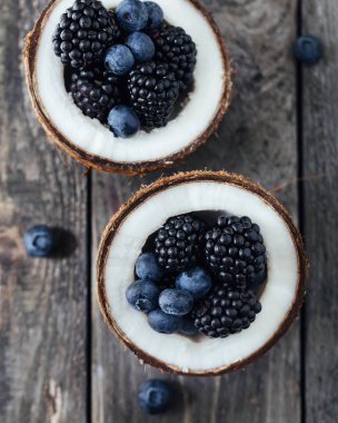 Ahşap bir arka plan üzerinde böğürtlen ve yaban mersini ile dolu 2 hindistan cevizi yarısı.