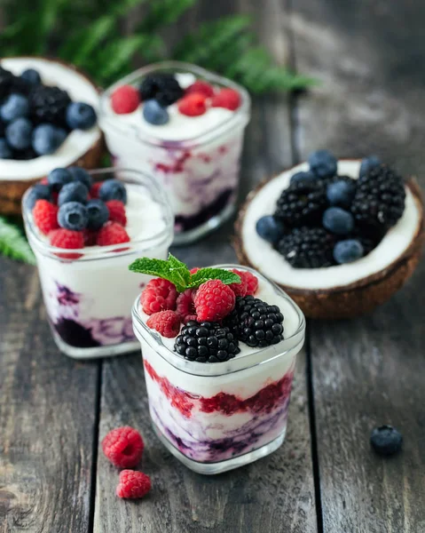 3 cups yogurt with raspberries, blueberries, blackberries on a dark wooden rustic background.