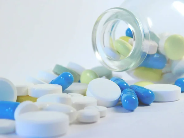 tablets, capsules, pills and pellets in a transparent glass medical flask on a light background.
