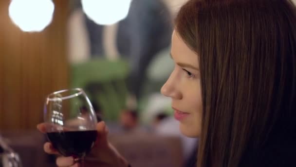 彼女の手に赤ワインのグラスを持つ魅力的な青い目の茶色の髪の女の子 女の子はバーでワインを手にして祝辞を述べている レストランでのアルコール 幸運を引き付ける少女 — ストック動画