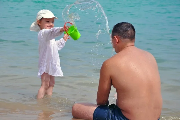 The girl pours water on her father. Splashes of water in the sea. Child and father on vacation. — Stock Photo, Image