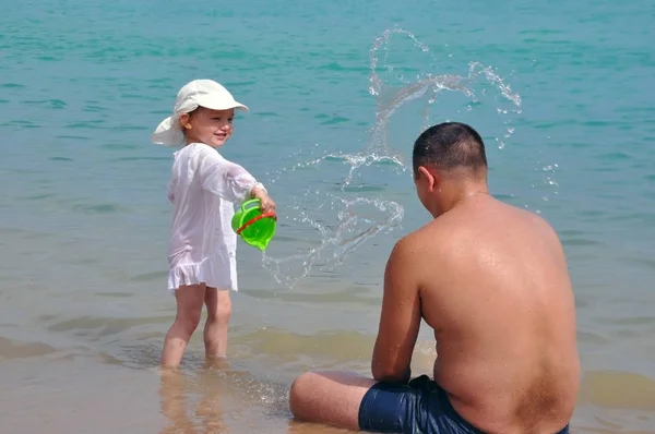 La chica derrama agua sobre su padre. Salpicaduras de agua en el mar. Niño y padre de vacaciones . —  Fotos de Stock