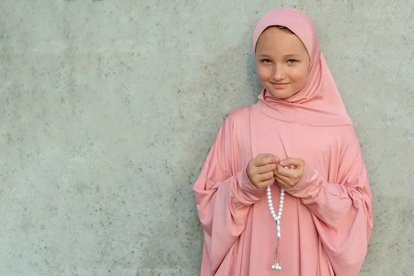 Ein Kind im rosafarbenen Hijab mit einer Perle in der Hand und Kopierraum. Menschen religiöser Lebensstil Konzept. — Stockfoto