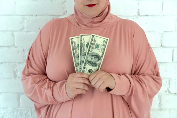 Junge muslimische Frau in rosa Hijab-Kleidung hält Bargeld in Dollarnoten und Rosenkranz in ihren Händen — Stockfoto