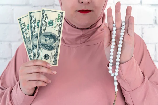 Weiße Frau mit blauen Augen in rosa Hijab mit Rosenkranz und Dollars auf weißem Hintergrund. — Stockfoto