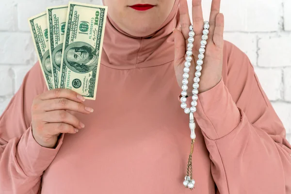 Weiße Frau mit blauen Augen in rosa Hijab mit Rosenkranz und Dollars auf weißem Hintergrund. — Stockfoto