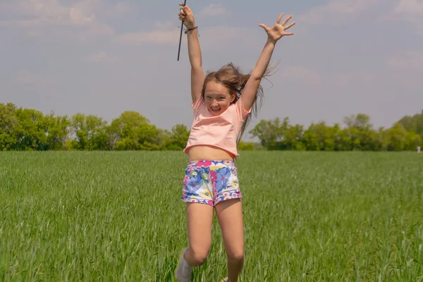 Happy girl with long hair holding a colored windmill toy in her hands raises her hand and jumps. — Stock Photo, Image