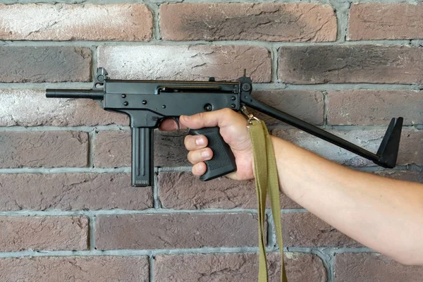 Subfusil PP-91 Kedr. Un hombre sostiene una ametralladora en su mano sobre el fondo de una pared de ladrillo marrón —  Fotos de Stock