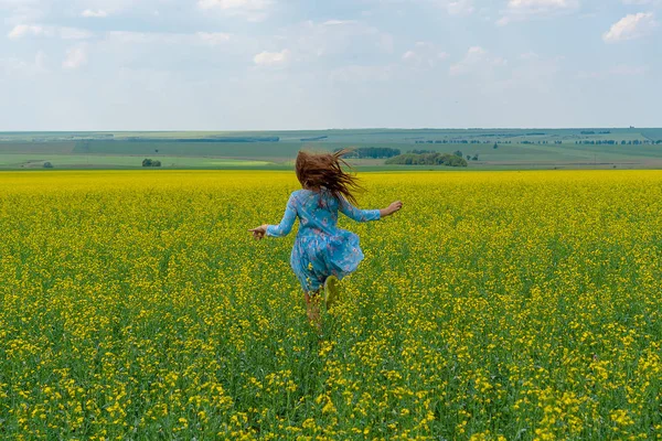 Uma menina feliz com cabelos longos atravessa um campo de flores amarelas. Cabelo desenvolver . — Fotografia de Stock