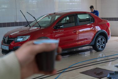 man drinking coffee while waiting for his car to wash. Car wash. Renault Logan Stepway. clipart