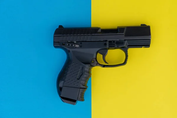 Image rapprochée du pistolet sur un fond multicolore. Pistolet noir sur fond jaune et bleu amusant . — Photo