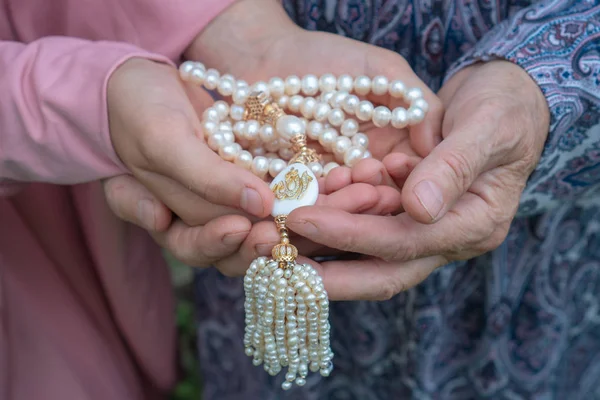Eine ältere Frau und ein kleines Mädchen halten einen schönen weißen Rosenkranz in der Hand. Hände einer alten Frau und eines kleinen Mädchens mit Perlenkranz in Großaufnahme. Religiöses Konzept — Stockfoto
