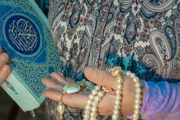 Μια ηλικιωμένη γυναίκα κρατά ένα όμορφο λευκό Ροζάριο και το Κοράνι. Τα χέρια ενός ηλικιωμένου με ένα ιερό βιβλίο και ένα κοντινό. Θρησκευτική αντίληψη — Φωτογραφία Αρχείου