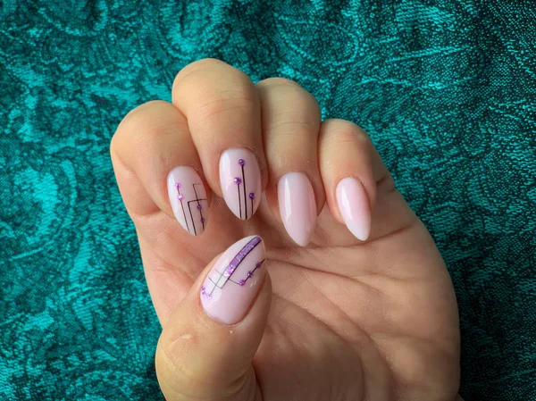 Stylish trendy female pink manicure. Pink manicure with with black geometric pattern on almond-shaped nails on a green background.