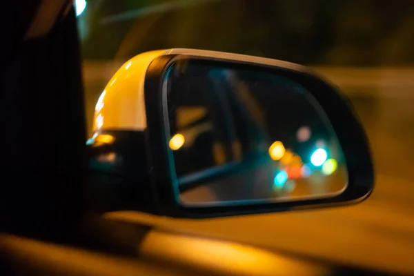 夜の道路で、車のサイドビューミラーの風景。●車のサイドミラーには夜市のライトが映し出される — ストック写真