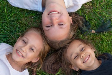 Üç kız kardeş yaz portresi. Sevimli kızlar çimenlerin üzerinde yatıyor ve gülümsüyorlar. gülümseyen çocuklar açık. Yaz kavramı.
