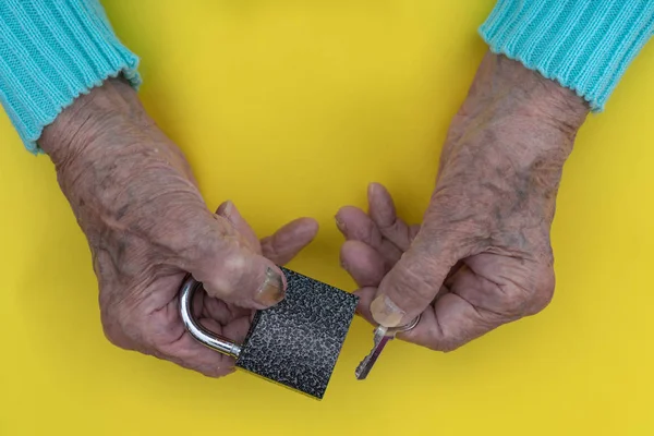 Händerna på en gammal kvinna 90 år närbild. Nyckeln och lås i händerna på en gammal kvinna på en gul bakgrund — Stockfoto