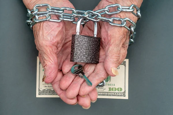 Les mains d'une vieille femme 90 ans de près. La clé et la serrure, 100 dollars entre les mains d'une vieille femme. Les mains de la vieille femme sont attachées avec une chaîne — Photo