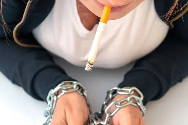 Woman\'s hands tied by chain with cigarette on a white background