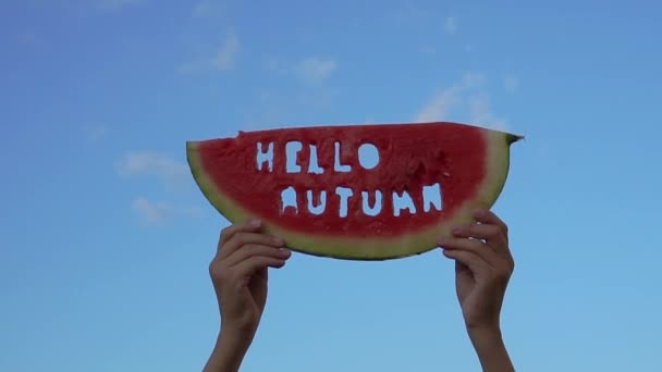 Кусок арбуза на фоне голубого неба. Дети держат в руках кусок арбуза с текстом Hello Autumn. Концепция осеннего времени — стоковое видео